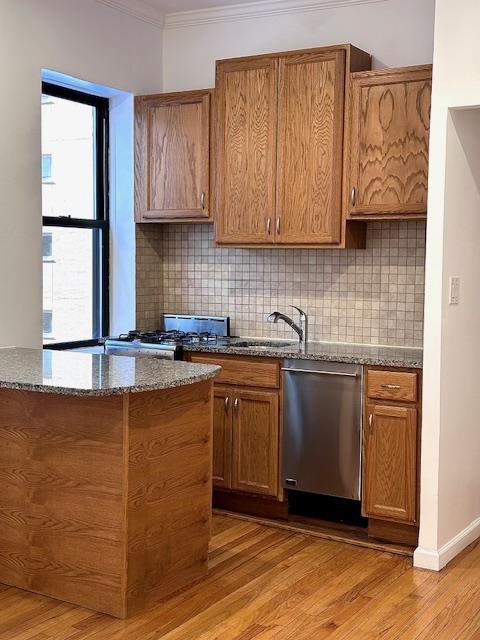 kitchen with light wood finished floors, dishwasher, ornamental molding, decorative backsplash, and dark stone countertops