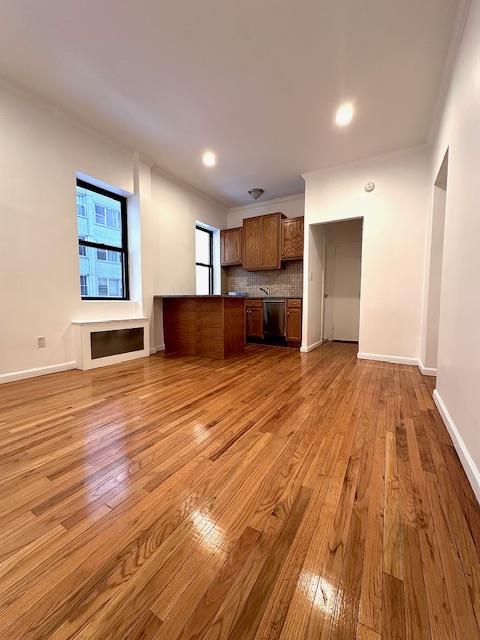 unfurnished living room with crown molding, light wood-type flooring, and baseboards