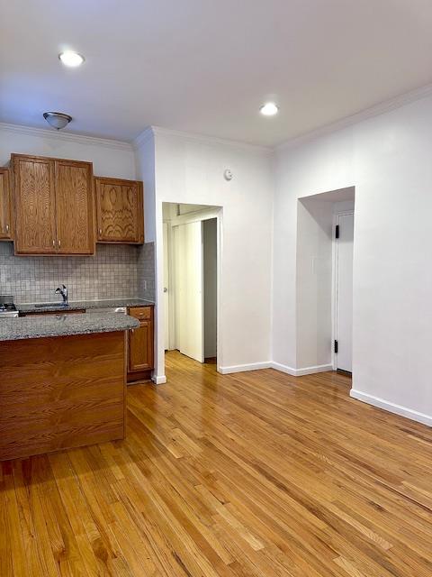 kitchen with tasteful backsplash, crown molding, baseboards, light wood-type flooring, and brown cabinets