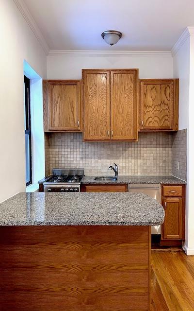 kitchen with ornamental molding, dark stone countertops, wood finished floors, stainless steel gas stove, and a sink