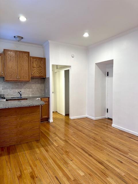 kitchen featuring brown cabinets, crown molding, decorative backsplash, light wood-type flooring, and baseboards
