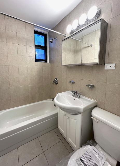 bathroom with tile patterned flooring, tile walls, toilet, shower / bathtub combination, and vanity