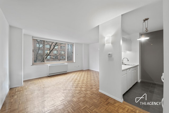 kitchen featuring decorative light fixtures, light countertops, radiator heating unit, white cabinets, and a sink