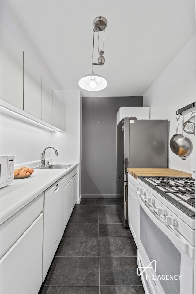 kitchen featuring decorative light fixtures, light countertops, white cabinets, a sink, and white appliances