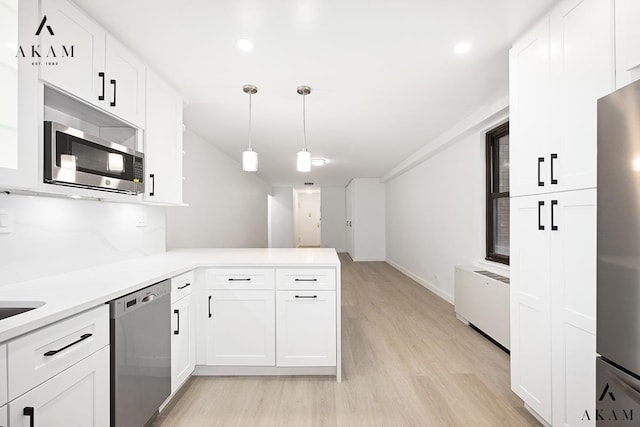 kitchen featuring stainless steel appliances, light countertops, radiator heating unit, white cabinetry, and a peninsula