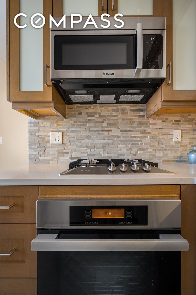 kitchen featuring light countertops, appliances with stainless steel finishes, brown cabinetry, and backsplash