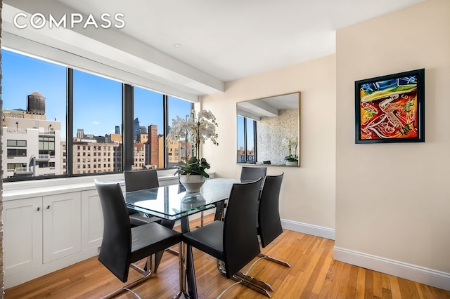 dining space featuring baseboards, light wood-type flooring, and a city view