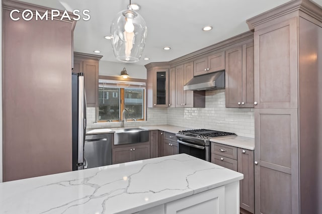 kitchen featuring light stone countertops, a sink, stainless steel appliances, under cabinet range hood, and tasteful backsplash