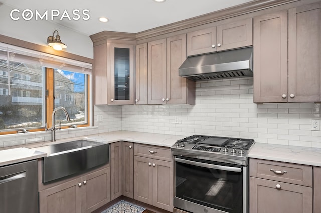 kitchen with a sink, decorative backsplash, glass insert cabinets, under cabinet range hood, and appliances with stainless steel finishes