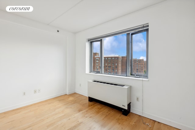 unfurnished room featuring radiator heating unit, wood finished floors, visible vents, and baseboards