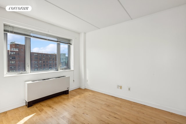 spare room featuring a city view, light wood finished floors, radiator, visible vents, and baseboards