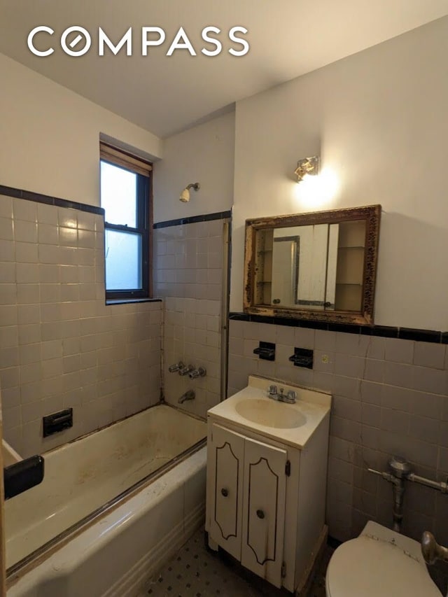 bathroom with toilet, shower / bathtub combination, tile walls, wainscoting, and vanity