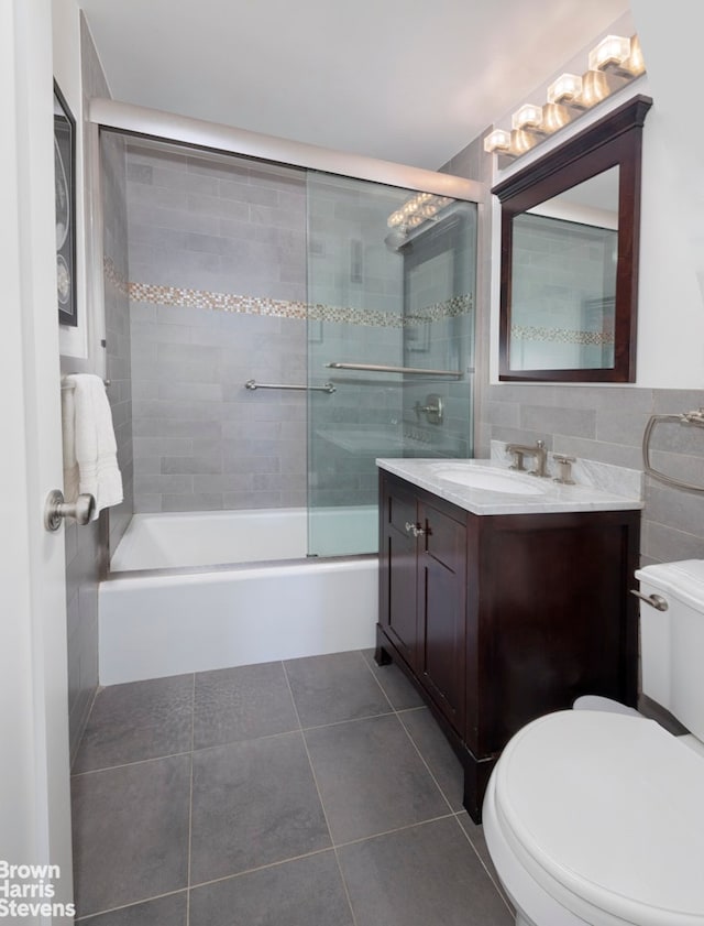 full bathroom featuring bath / shower combo with glass door, toilet, tile patterned floors, vanity, and tile walls