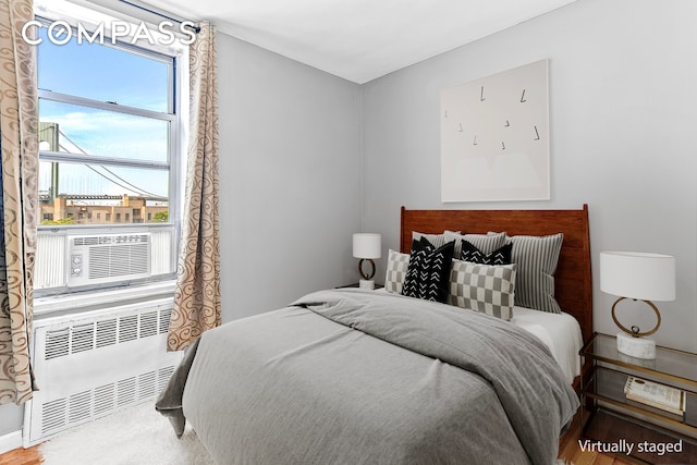 bedroom with cooling unit, radiator, and wood finished floors