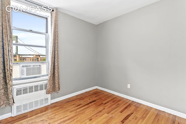 empty room featuring cooling unit, baseboards, radiator, and wood finished floors