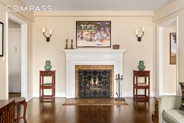 living area with baseboards, dark wood-style flooring, and a lit fireplace