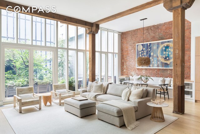 living room with wood finished floors, brick wall, a high ceiling, expansive windows, and beamed ceiling