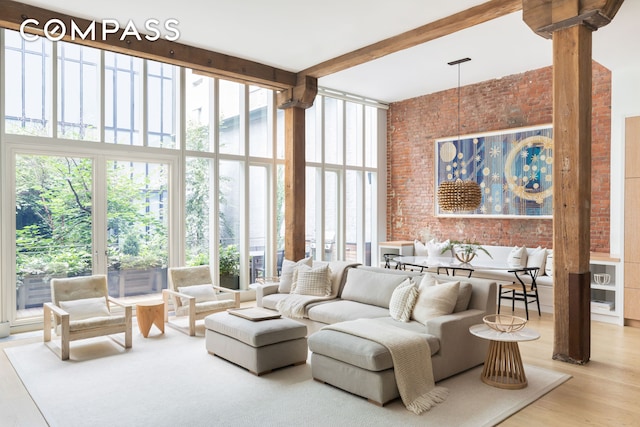 living room with brick wall, expansive windows, beam ceiling, a high ceiling, and wood finished floors