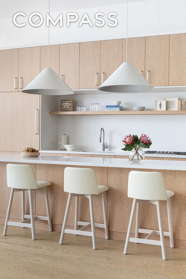 kitchen with a breakfast bar, open shelves, a sink, light brown cabinetry, and light wood-style floors