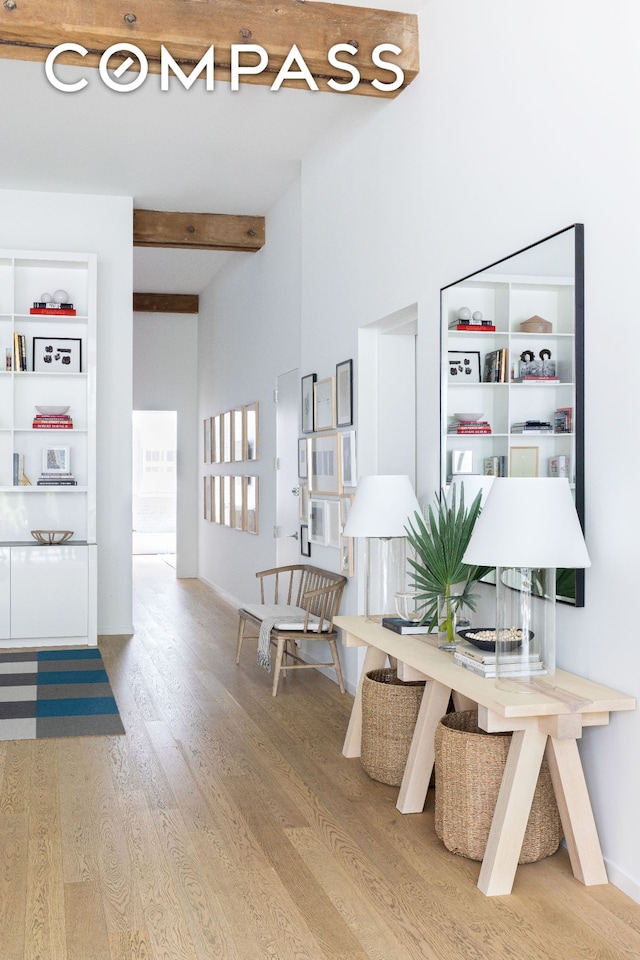 hallway featuring beamed ceiling, wood finished floors, and baseboards