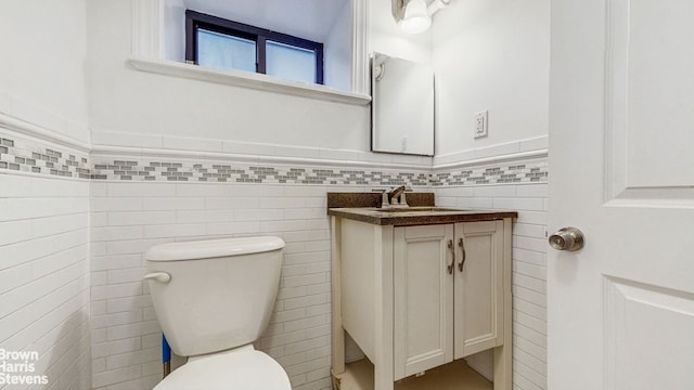 half bathroom with toilet, tile walls, wainscoting, and vanity