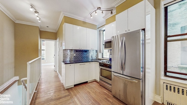 kitchen featuring decorative backsplash, radiator, light wood-type flooring, rail lighting, and appliances with stainless steel finishes