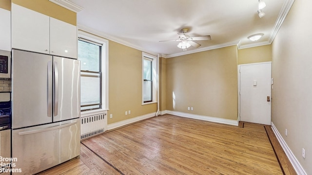 interior space with crown molding, light wood-style flooring, radiator, stainless steel appliances, and a ceiling fan