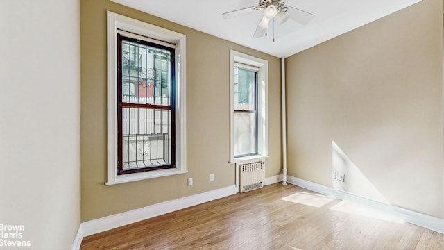 empty room with baseboards, ceiling fan, radiator heating unit, and wood finished floors