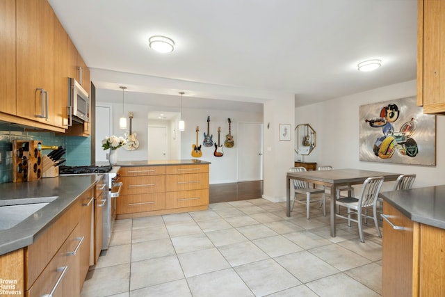 kitchen with a peninsula, backsplash, light tile patterned flooring, decorative light fixtures, and appliances with stainless steel finishes