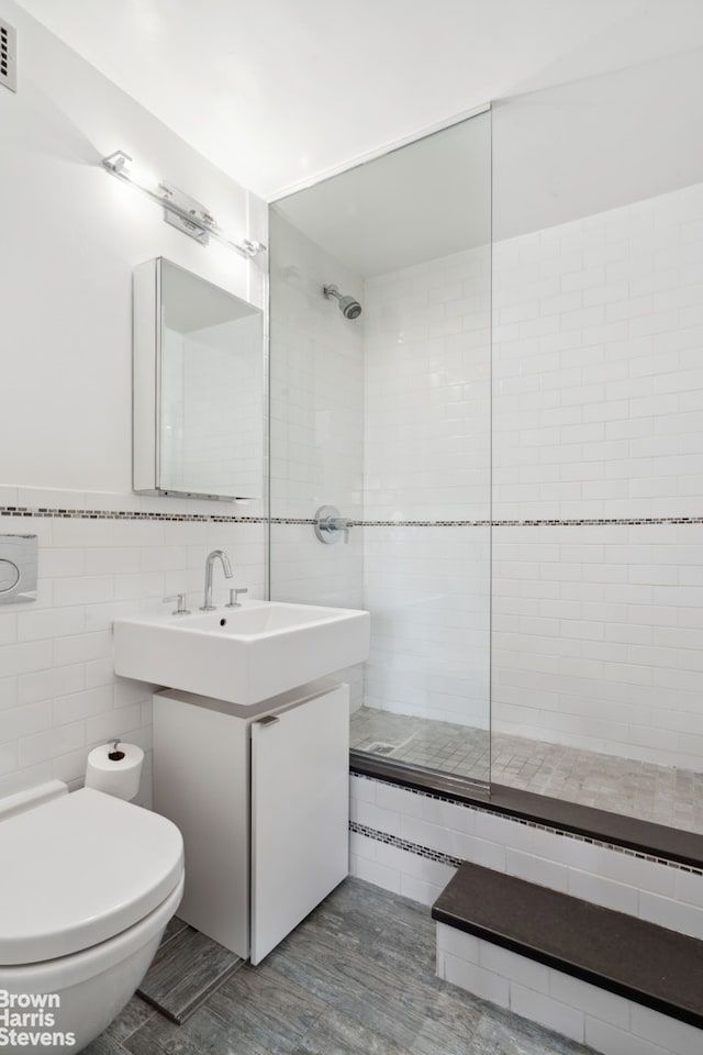 bathroom with tile walls, visible vents, toilet, a sink, and tiled shower