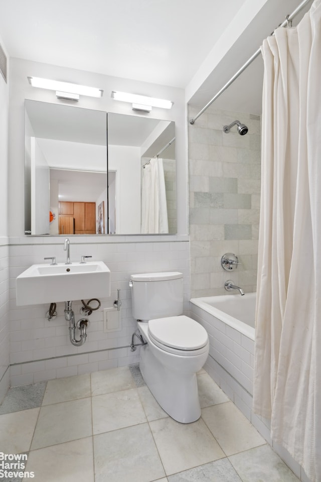 bathroom featuring tile patterned floors, toilet, tiled shower / bath combo, tile walls, and a sink
