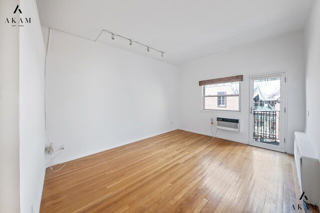 unfurnished room with an AC wall unit, light wood-type flooring, and track lighting