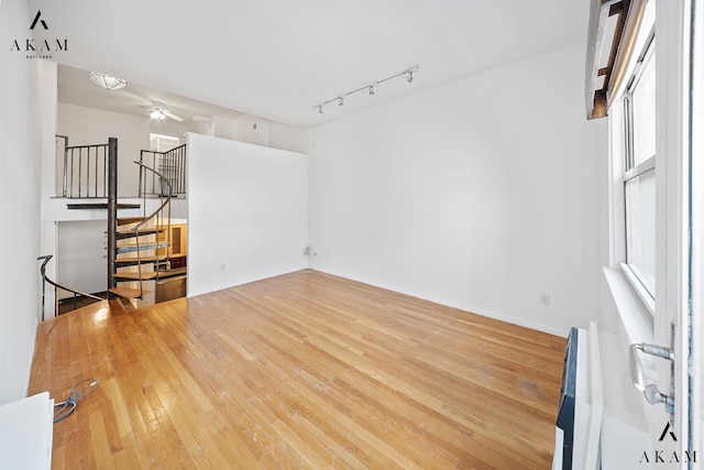 unfurnished living room with hardwood / wood-style flooring, ceiling fan, stairs, and track lighting