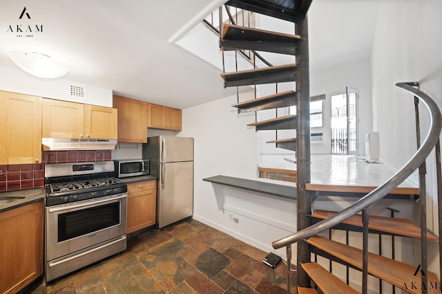 211 Thompson St Unit 4-C, New York City, NY 10012 - kitchen featuring appliances with stainless steel finishes, under cabinet range hood, dark stone finish floors, backsplash, and baseboards