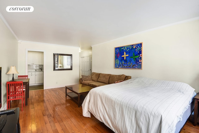 bedroom with crown molding, visible vents, hardwood / wood-style floors, a sink, and baseboards