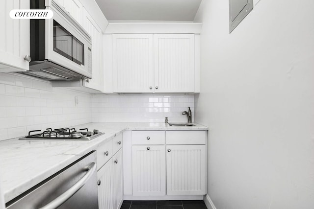 kitchen featuring light stone counters, dark tile patterned floors, white cabinetry, appliances with stainless steel finishes, and backsplash