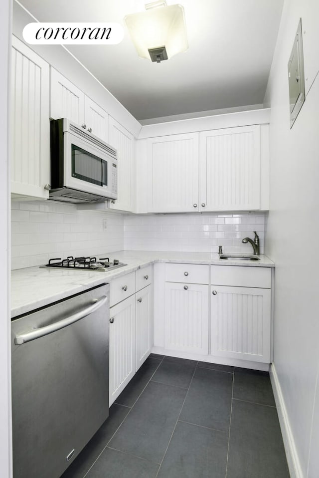 kitchen featuring a sink, stainless steel appliances, dark tile patterned floors, white cabinetry, and backsplash