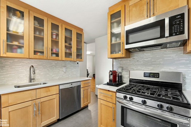 kitchen featuring stainless steel appliances, glass insert cabinets, a sink, and backsplash