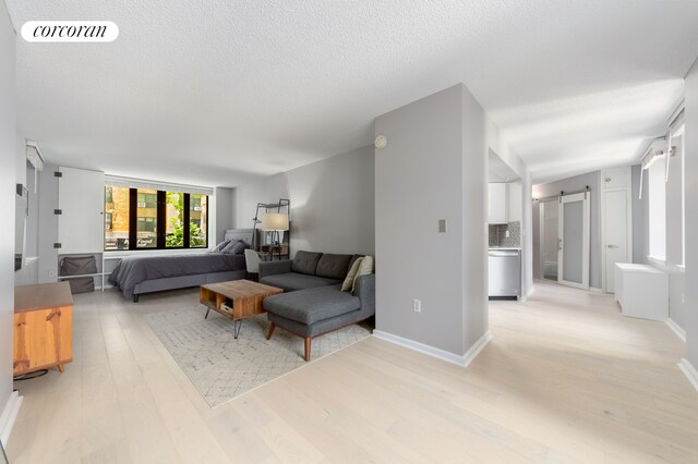 living area featuring light wood-type flooring, visible vents, a textured ceiling, a barn door, and baseboards