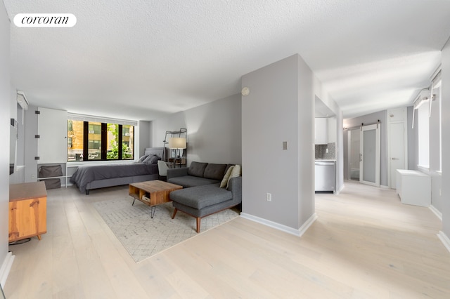 bedroom featuring visible vents, light wood-style flooring, a textured ceiling, a barn door, and baseboards