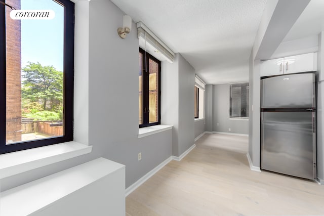 corridor with light wood-style flooring, baseboards, and a textured ceiling