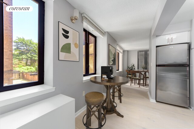 corridor with light wood-style flooring, baseboards, and a textured ceiling