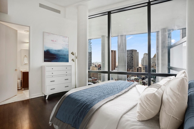 bedroom with floor to ceiling windows, a city view, visible vents, connected bathroom, and wood finished floors