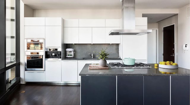 kitchen featuring double oven, stainless steel gas cooktop, island range hood, and modern cabinets