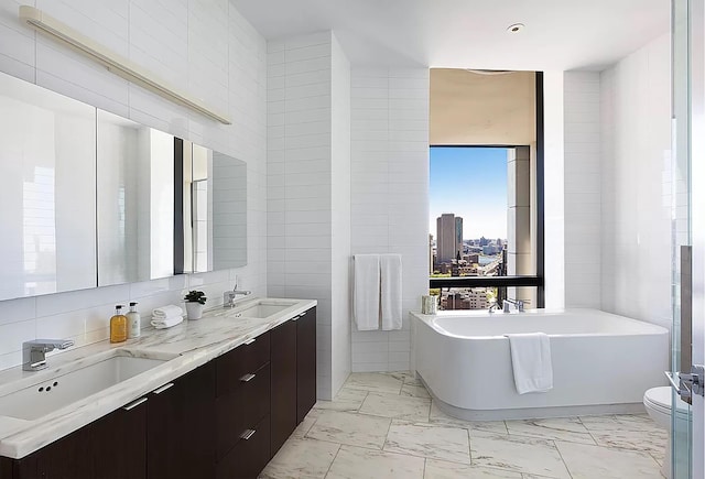 bathroom with marble finish floor, a soaking tub, a sink, and tile walls