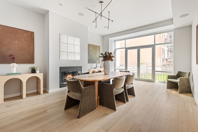 dining area with a glass covered fireplace, a notable chandelier, light wood-style floors, and french doors