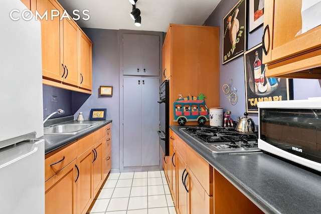 kitchen featuring light tile patterned flooring, oven, a sink, freestanding refrigerator, and dark countertops