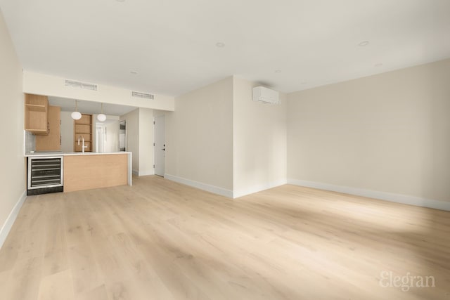 unfurnished living room with visible vents, beverage cooler, light wood-style floors, and baseboards