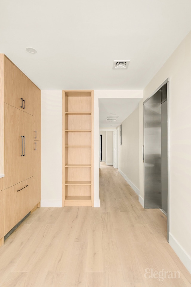 corridor featuring light wood-style flooring, elevator, baseboards, and visible vents