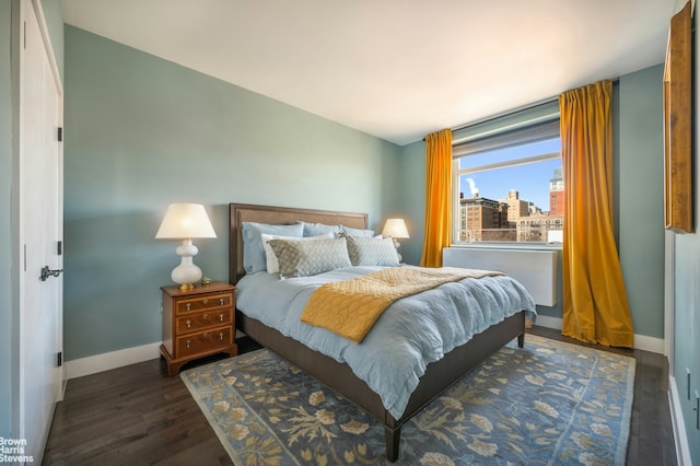 bedroom with a view of city, wood finished floors, and baseboards